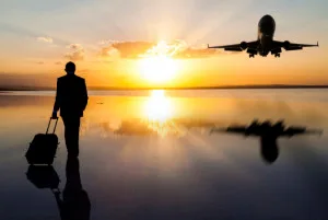 fear of flying course - pilot standing with hand lugguage looking at sunset with plane taking off to the right