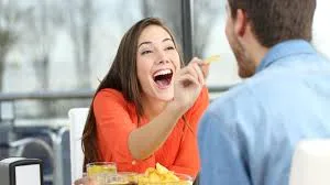 Attractive woman offering a fork of her food to male companion across a restaurant table after successful hypnotherapy for emetophobia