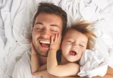smiling man cuddling toddler with toddler's hand on his mouth after hypnotherapy for emetophobia